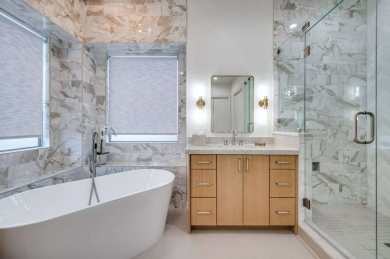 Luxury bathroom by Make Ready Home with marble walls, freestanding tub, glass shower, and wood vanity.