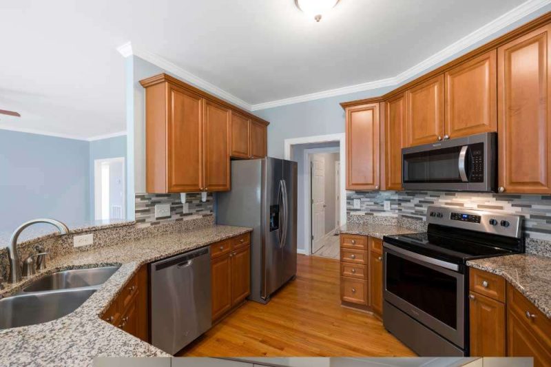Make Ready Home cabinet painting or replacement in Fort Worth kitchen featuring warm wood cabinets, granite counters, and stainless steel.